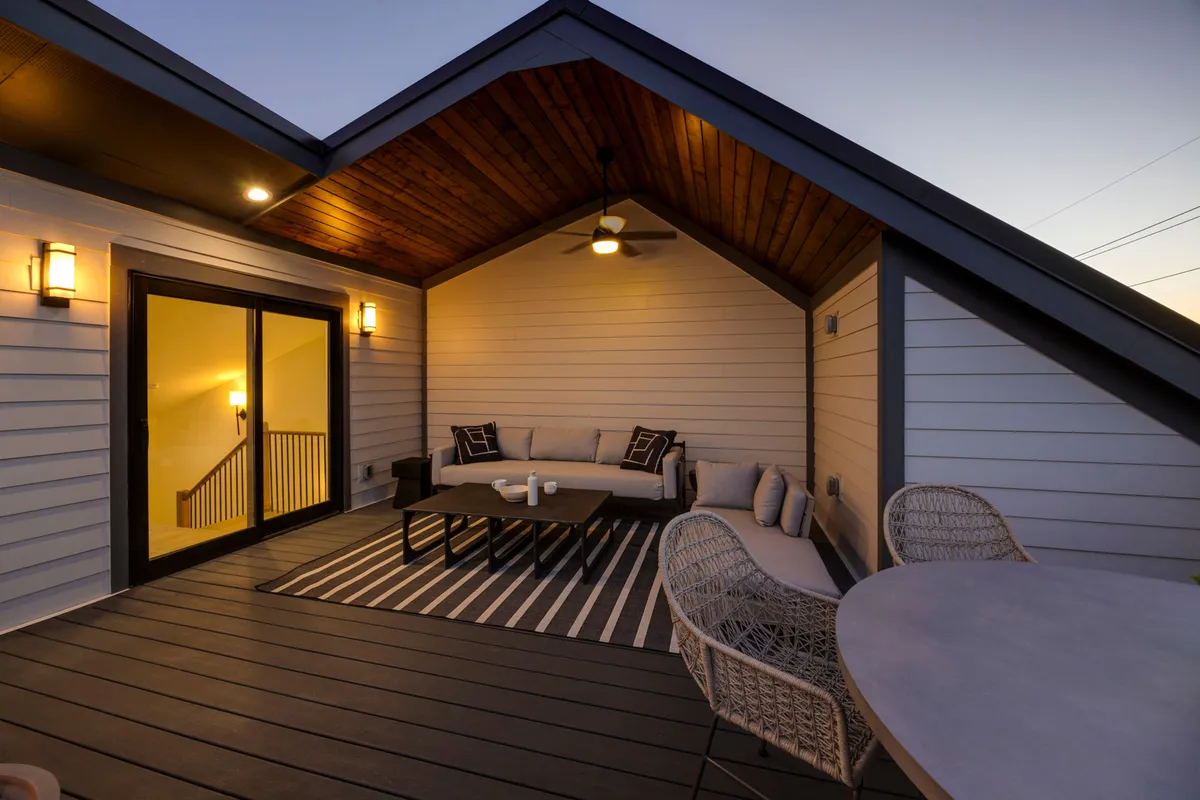 This exterior image captures a stylish rooftop setting with a plush sofa set, coffee table, outdoor dining table, decorative cushions, and a rug. The tranquil scene hints at both relaxation and entertaining, with space for gathering and sunset watching.