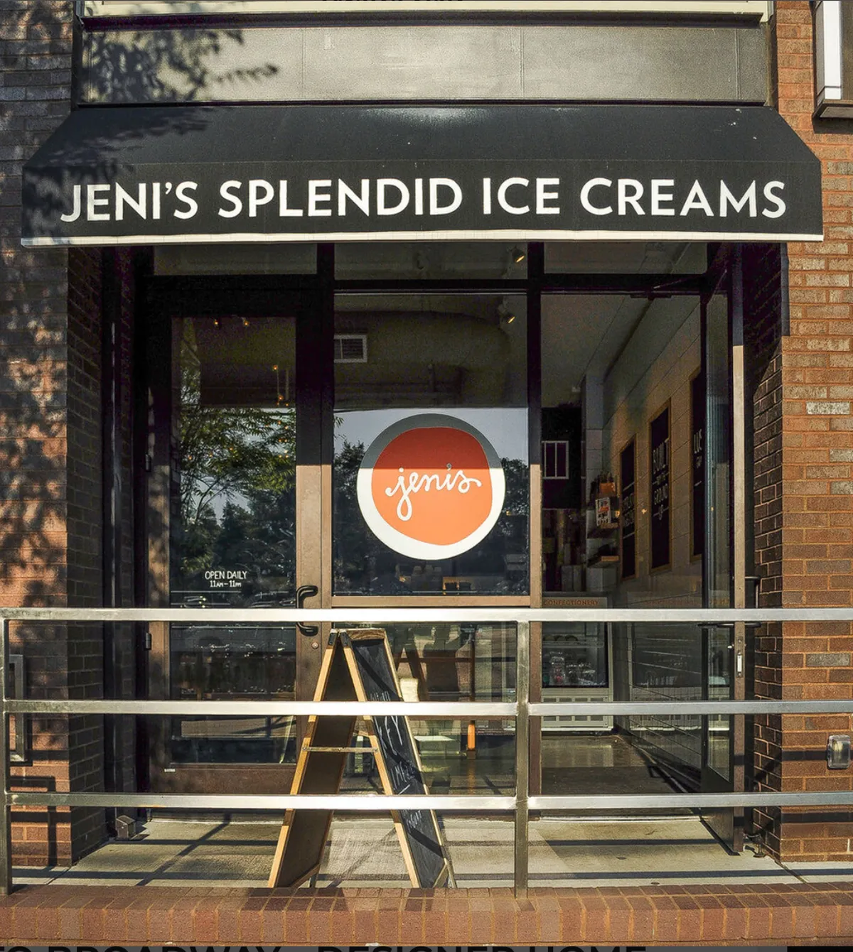 A cheerful storefront for Jeni's Splendid Ice Creams, complete with a welcoming sign and a sidewalk menu board, encourages passersby to stop for a treat. The scene is lively and inviting, hinting at sweet moments shared during family adventures.