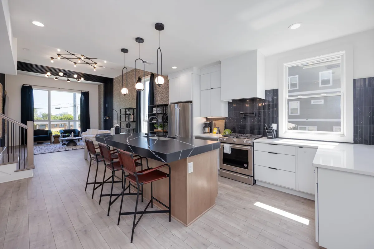 A spacious, contemporary kitchen featuring an oversized island with comfortable seating, stylish pendant lights, stainless steel appliances, and large windows that flood the space with natural light. The layout invites conversation and is ideal for cooking, casual bites, or hosting gatherings.