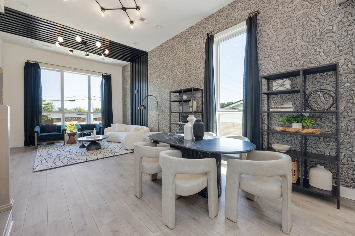 A contemporary dining area connected with a comfortable seating space, adorned with a large window allowing natural light to fill the room. The elegant dining table is ready for gatherings, and the overall mood is welcoming and sophisticated—ideal for memorable meals and socializing.