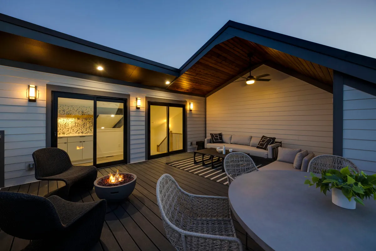 The image spotlights a cozy fire pit surrounded by a comfortable outdoor seating area, adjacent to large glass doors. The lighting suggests dusk or evening, enhancing the sense of warmth and intimacy.