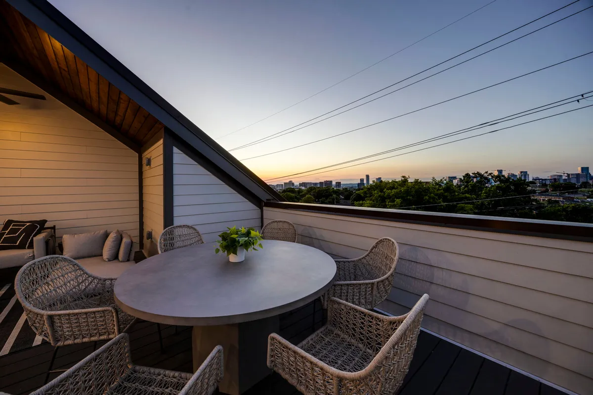 This exterior rooftop image features a round table with woven chairs, a potted plant, and an unmistakable city skyline backdrop. The mood is calm and inviting, with a clear view of sunset skies over Nashville.